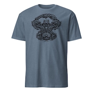 May include: A blue short-sleeved t-shirt featuring a detailed black graphic. The graphic depicts a stylized creature with wings and a central figure, surrounded by intricate patterns and shapes. The shirt is made of a soft material.