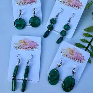May include: Four pairs of green malachite earrings on white cards. The earrings have various shapes, including circles, ovals, and elongated rectangles. Each card displays the text "SONOMA SKY DESIGNS BY AMBER".