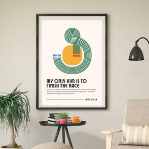 May include: Framed art print with the text "MY ONLY AIM IS TO FINISH THE RACE" in black font. The artwork features a green and orange abstract design. The print is displayed on a beige wall, with a black frame.