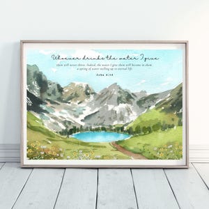 May include: Framed watercolour print depicting a mountain landscape with a lake. The artwork features a quote from John 4:14 in elegant script. The scene includes mountains, a lake, and a path. The frame is light wood.