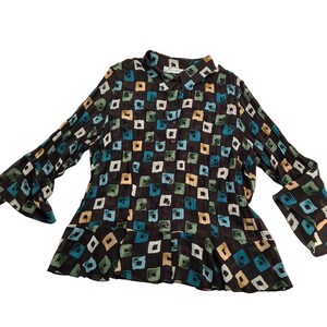 May include: A long-sleeved button-down shirt in a dark brown fabric featuring a repeating pattern of small, hand-painted style squares in shades of teal, light green, and beige. The garment has a classic collar and a flared, ruffled hemline.