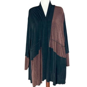 May include: A long-sleeved cardigan in black and brown, displayed on a mannequin. The garment features a draped neckline and panels of contrasting colors and textures. The sleeves and lower sections have brown accents.