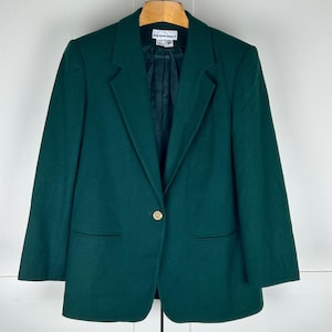 Puede incluir: Un blazer de color verde bosque oscuro sólido con un cierre de un solo botón dorado en el centro, solapas con muescas y dos bolsillos ribeteados delanteros. El interior está forrado con tela oscura y tiene una etiqueta blanca con BLAIR.