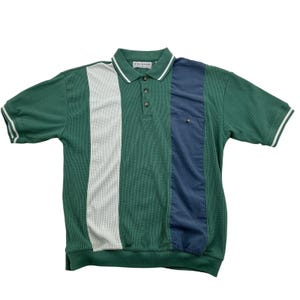 May include: A short-sleeve polo shirt with a waffle-knit texture, featuring a color-blocked design in forest green, white, and navy blue. The shirt has a collared neckline with three buttons, white striped trim on the sleeves, and a small chest pocket.