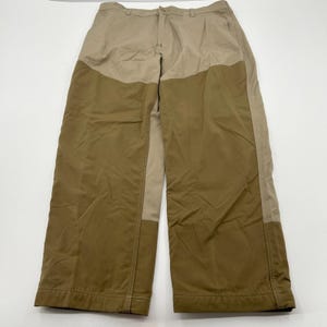 Peut inclure: Pantalon bicolore beige et vert olive. Ce pantalon à jambes larges est doté d'une fermeture boutonnée et zippée. Le design intègre un motif color-block, avec des panneaux vert olive à l'avant et beige à l'arrière. Fabriqué dans un tissu résistant.