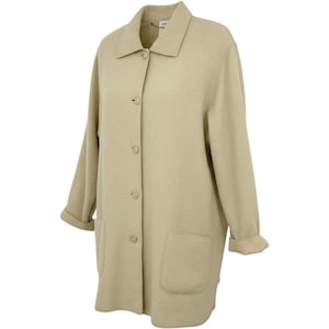 May include: A beige long-sleeved coat featuring a classic collar, a front button-down closure with four visible buttons, and two large patch pockets on the lower front. The sleeves have folded cuffs, and the fabric has a smooth, solid texture.