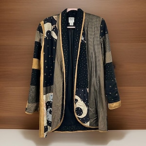 Op de afbeelding: Een patchwork jas met verschillende patronen en kleuren. De jas heeft een mix van zwarte, gouden en bruine stoffen met geometrische en paisley ontwerpen. De jas heeft een kraag en is open aan de voorkant.