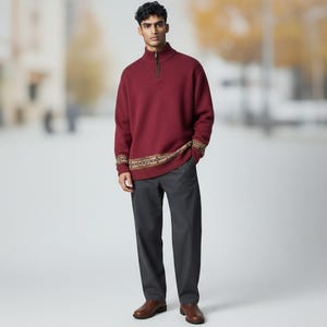May include: A deep red quarter-zip sweater featuring a high collar and a decorative patterned band along the hem and cuffs, paired with charcoal gray trousers and brown leather shoes. The sweater has a textured knit finish and a metal zipper.
