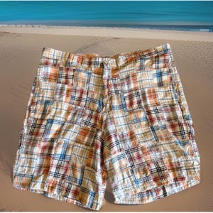 May include: Patchwork shorts in a plaid pattern with a button closure. The shorts feature a mix of colors including white, orange, blue, and red. The shorts are made of a lightweight fabric, perfect for warm weather.