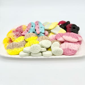 May include: A white oval platter filled with a variety of colorful candies. The candies include pink, blue, yellow, and green shapes, some with the word "RIBS" printed on them. The candies are arranged on a white background.