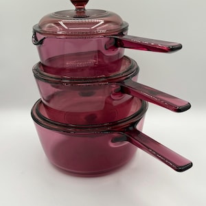 May include: A set of three ceramic mugs with a speckled, cream-colored glaze. Each mug features a different hand-painted floral design in shades of blue, green, and yellow. The mugs have a simple, rounded shape and a comfortable handle.