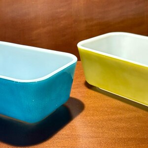 Peut inclure: Deux plats à four rectangulaires, un bleu turquoise et un jaune. Les deux ont un intérieur blanc et reposent sur une surface en bois. Les plats sont probablement en verre ou en céramique et sont vintage. Chaque plat mesure environ 20 cm de long.
