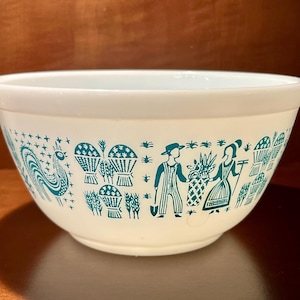 以下が含まれることがあります： 白のパイレックスミキシングボウル、ターコイズ色の収穫デザイン。ボウルは、様式化された人物、作物、雄鶏の繰り返し模様が特徴です。ボウルは丸く、広い縁と滑らかで光沢のある仕上がりです。