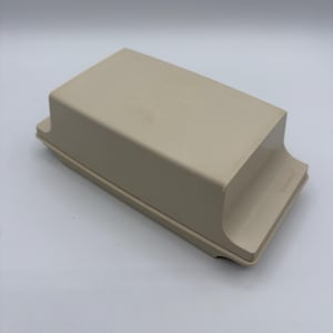 May include: A rectangular, beige-coloured plastic butter dish with a lid. The lid features a smooth, solid surface and a slightly flared base. The word Tupperware is embossed on the side of the lid, indicating the brand of this kitchen storage container.
