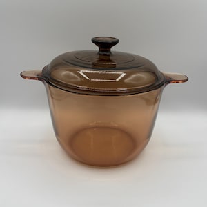 Peut inclure: Une marmite en verre ambré translucide avec un couvercle assorti. La marmite présente deux poignées latérales intégrées et un bouton central sur le couvercle. Le verre est lisse et de couleur uniforme, avec une base arrondie et une large ouverture.
