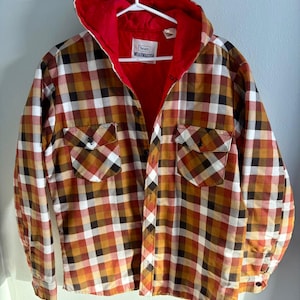 May include: A vintage Sears Wearmaster plaid shirt with a red quilted lining and hood. The shirt features a button-down front, two chest pockets, and a classic plaid pattern in shades of brown, orange, and white. The tag reads "Sears Wearmaster".