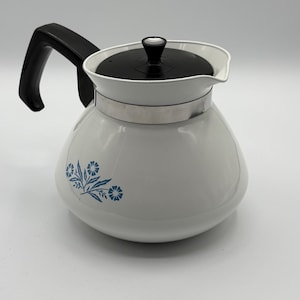May include: White coffee pot with a black handle and lid. The pot features a blue floral design. The pot is made of ceramic or enamel and has a silver band around the middle.