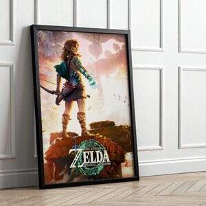 May include: Framed art print featuring a character from "The Legend of Zelda: Tears of the Kingdom." The artwork depicts a figure with a bow and arrow, standing on a rock formation. The title is displayed in a teal and white circular design.