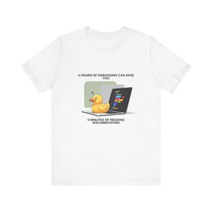 May include: White t-shirt with a graphic of a yellow rubber duck on a laptop displaying code. The text reads, "6 hours of debugging can save you, 5 minutes of reading documentation."