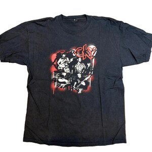 May include: Black t-shirt featuring a band graphic with the word "CKY" in red and white. The graphic depicts band members playing instruments against a red backdrop. The shirt is made of a soft material.