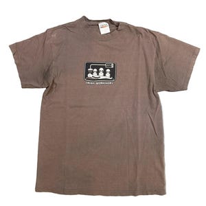 May include: Brown t-shirt with a black and white graphic of three aliens in a lab setting. The text "(ALIEN WORKSHOP)" is below the graphic. The shirt has a crew neck and short sleeves.