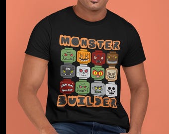 May include: Black t-shirt with the words "MONSTER BUILDER" in orange block letters. The shirt features a grid of colorful monster faces, each designed to resemble building blocks, in various colors and expressions.