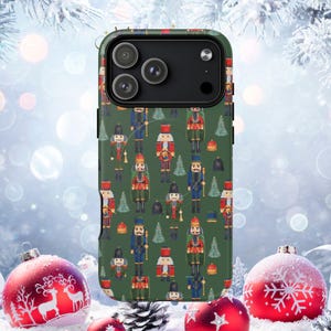 Op de afbeelding: Een groene telefoonhoes met een herhalend patroon van speelgoed notenkrakersoldaten en kerstbomen. De hoes heeft een camera-uitsparing en is omgeven door feestelijke vakantiedecoraties.
