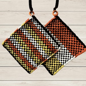May include: Two square potholders featuring a woven checkerboard pattern in alternating colors of black, white, yellow, and orange. Each potholder is finished with a black border and includes a small orange ring at the top for hanging purposes.