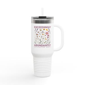 May include: White travel mug with a handle and a straw. The mug features the words "EXCEEDINGLY ABUNDANTLY" with a floral design. The mug is designed to hold hot or cold beverages.