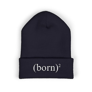 May include: A navy blue beanie with the white text "(born)²" embroidered on the folded brim. The hat is made of a soft material and is designed to keep the head warm. This winter hat is a stylish accessory.