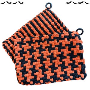 May include: Two square woven potholders featuring a black and orange checkered pattern. Each potholder is constructed from thick, interlocking fabric loops and includes a small black circular loop at the top corner for convenient hanging storage.