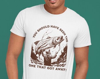 May include: White t-shirt featuring a brown graphic of a fisherman catching a large fish. The text "YOU SHOULD HAVE SEEN THE ONE THAT GOT AWAY!" is printed above and below the graphic. The shirt is made of a soft, comfortable material.