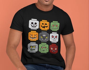 May include: Black t-shirt featuring a grid of nine cartoon monster faces, each resembling a building block. The faces include a skull, jack-o'-lantern, and various green, gray, and red monsters. The shirt is worn by a person.