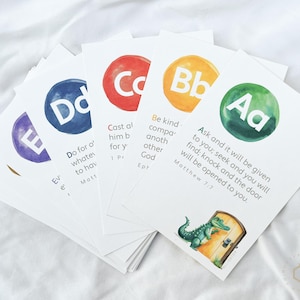 Può includere: Un gruppo di biglietti bianchi con cerchi ad acquerello colorati con lettere dell'alfabeto. Ogni biglietto ha una lettera diversa e un versetto biblico associato. Un biglietto presenta un'illustrazione di un alligatore.