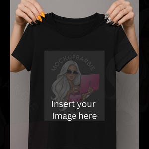 May include: Black t-shirt with a graphic on the front featuring a woman with sunglasses holding a pink laptop. The graphic is inside a gray square with the text "mockupbarbie" and "Insert your Image here".