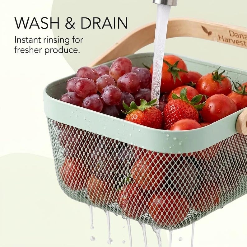 May include: A light green mesh colander basket with a wooden handle, filled with red grapes and tomatoes being rinsed under a stream of water. The basket features the text WASH & DRAIN and Instant rinsing for fresher produce on the side.