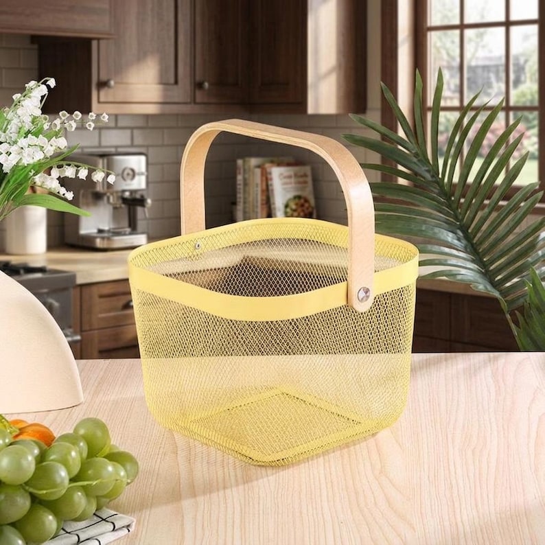 May include: A square-shaped storage basket featuring a bright yellow fine wire mesh body and a smooth, light-toned wooden handle attached with silver-colored metal rivets on each side. The basket has a wide opening and a flat, stable base.