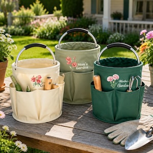 May include: Three cylindrical canvas garden tool bags with metal handles and black grips. The bags are cream, sage green, and dark green. Each features a floral graphic and text reading Mom's Garden or Martha's Garden with exterior pockets.