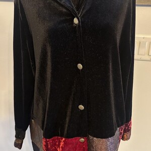 May include: A long-sleeved black velvet button-down shirt featuring a pointed collar and a hemline panel decorated with a patchwork of red, purple, and gold patterned fabric. The shirt includes silver-toned buttons down the front center.