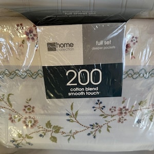 May include: A full sheet set in a cotton blend with a smooth touch, packaged in clear plastic. The fabric features a floral pattern with small pink and blue flowers on a white background. The label displays the text 200, home collection, and full set.