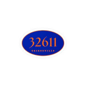 Puede incluir: Adhesivo ovalado con fondo azul y texto naranja. El número "32611" está en la parte superior y la palabra "gainesville" en la parte inferior. La pegatina tiene un borde blanco con un contorno naranja.
