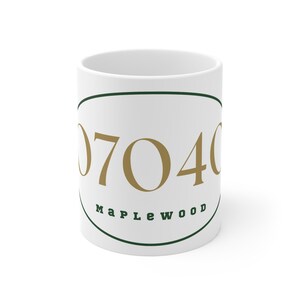 May include: White ceramic mug with the number "07040" in gold lettering inside a green oval, with "Maplewood" in green below. The mug is a standard size and shape.