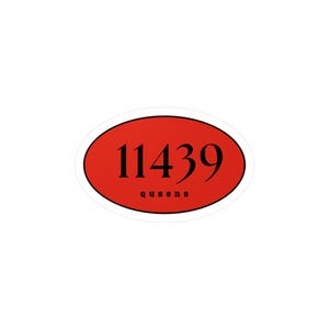 May include: An oval sticker with a red background and white border. The sticker features the number "11439" in black, with the word "queens" in a smaller black font below the numbers.