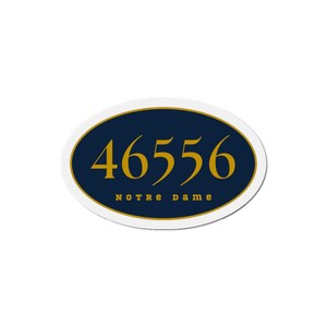 May include: An oval sticker with a white border. The center features a navy blue background with the gold numbers "46556" and the words "NOTRE DAME" in gold lettering. The sticker has a gold border around the navy blue oval.