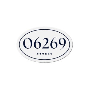 May include: An oval-shaped white sticker with a navy blue border. The sticker features the number "06269" in navy blue, with the word "STORRS" printed below the number in the same color.