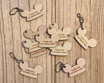 Könnte beinhalten: Eine Sammlung von Holzschlüsselanhängern in Form eines Mäusekopfes. Jeder Schlüsselanhänger trägt die Gravur "THANK YOU FOR MAKING MAGIC". Die Schlüsselanhänger sind hellbraun und haben eine silberne Kette.