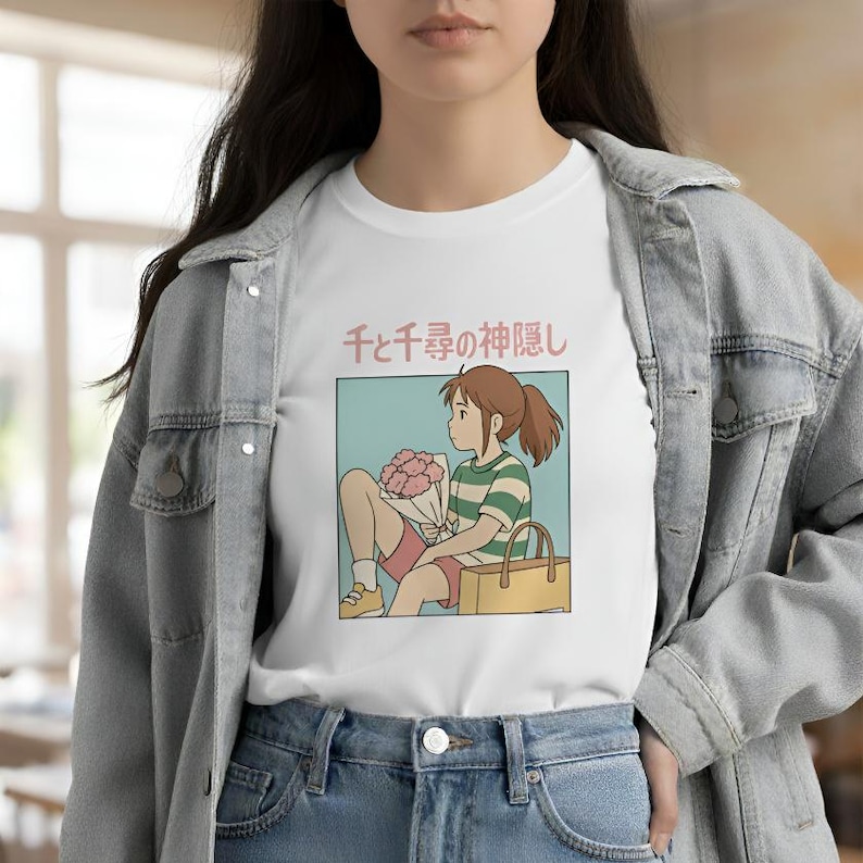 Puede incluir: Camiseta blanca con una ilustraci&oacute;n de estilo anime de una ni&ntilde;a sosteniendo flores y una bolsa. La ni&ntilde;a lleva una camiseta a rayas verdes y blancas y pantalones cortos rojos. Texto japon&eacute;s encima de la ilustraci&oacute;n.