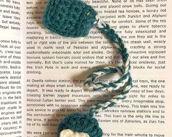 May include: Handmade teal crochet bookmark with a white and teal twisted cord and a white bow accent. The bookmark is designed to be placed on a book page.