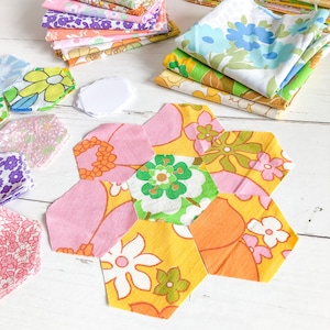 May include: A colourful patchwork hexagon quilt block with pink, yellow, orange, green and white floral fabric. The block is made up of six individual hexagons.