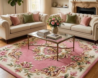 May include: A rectangular area rug featuring a pink center and a cream-colored border, decorated with a raised, three-dimensional floral pattern in shades of pink, yellow, and green, with intricate scrollwork and carved detailing throughout.